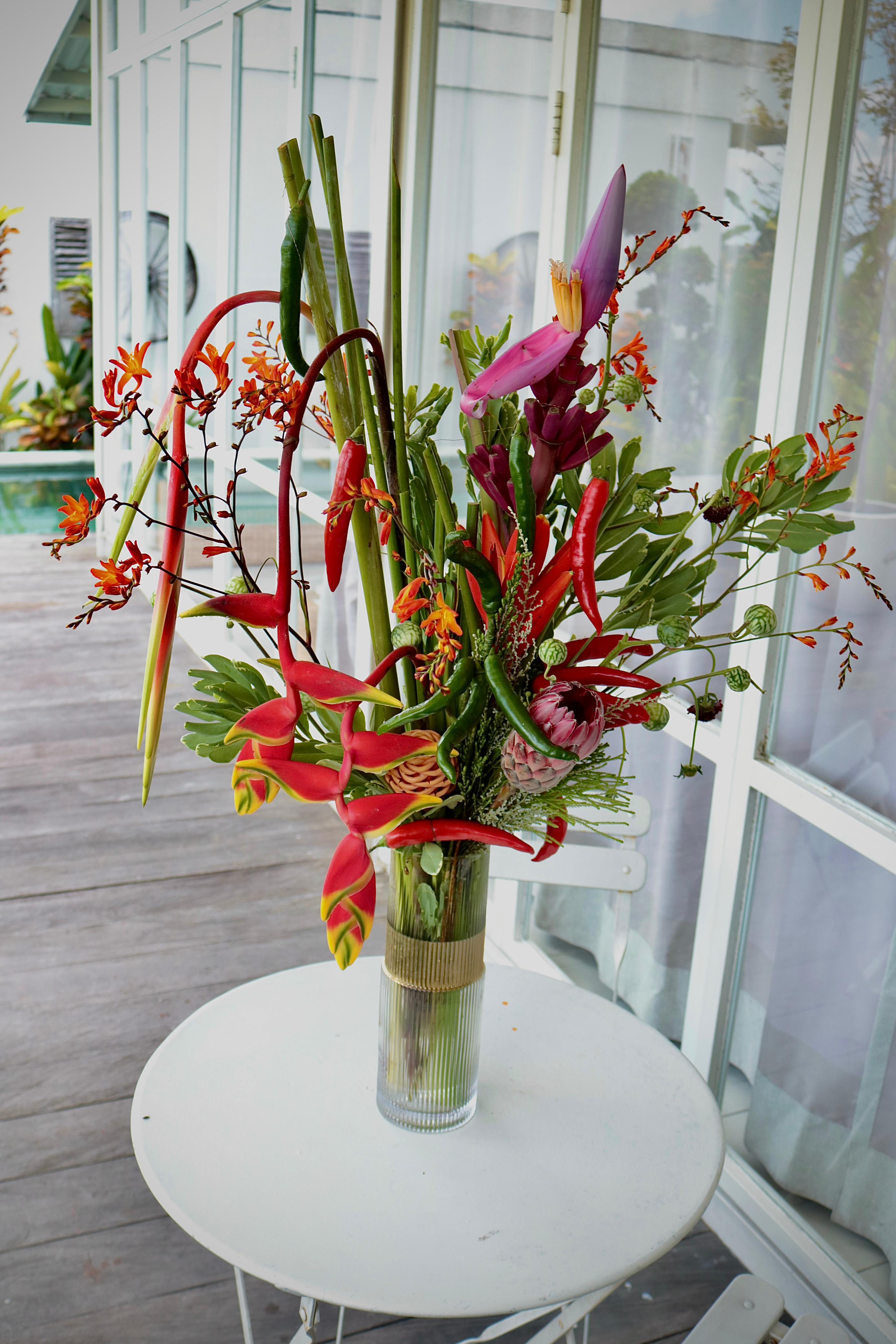 Colorful floral arrangement in a vase on a white table with a glass door in the background
