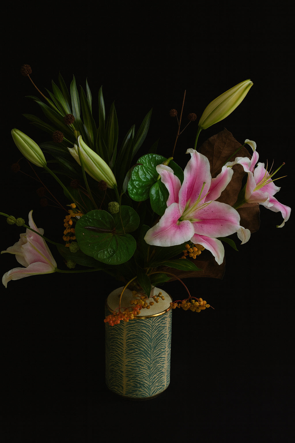 Bouquet of pink lilies and green leaves in a decorative vase on a black background