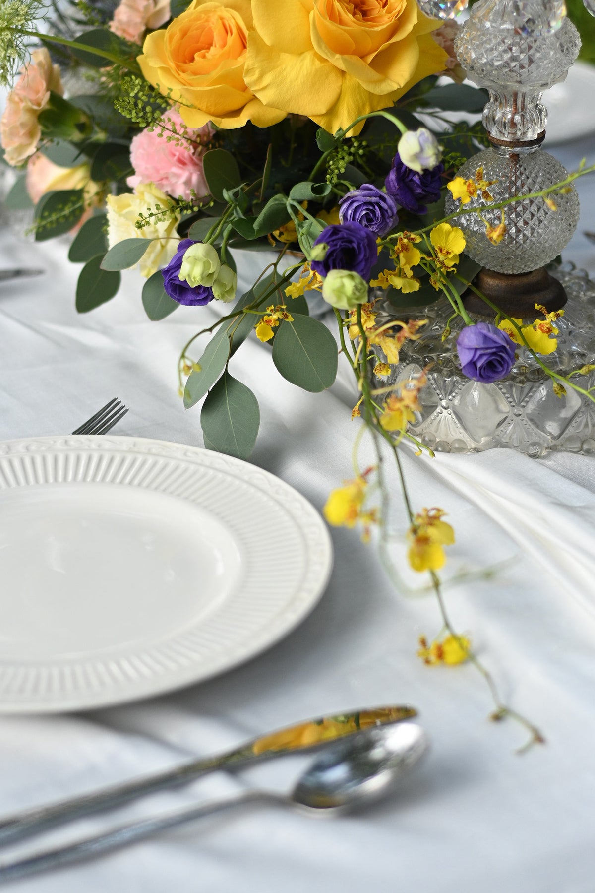 Table setting with flowers, plates, and cutlery on a white tablecloth.